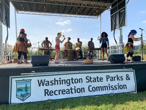 Photo depicting the group Kouyate Arts performing on a stage with a white banner that reads, "Washington State Parks & Recreation Commission."