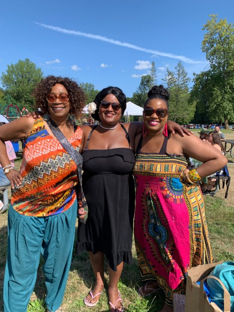Photo depicting three Black-presenting women wearing sunglasses in a park on a sunny day.